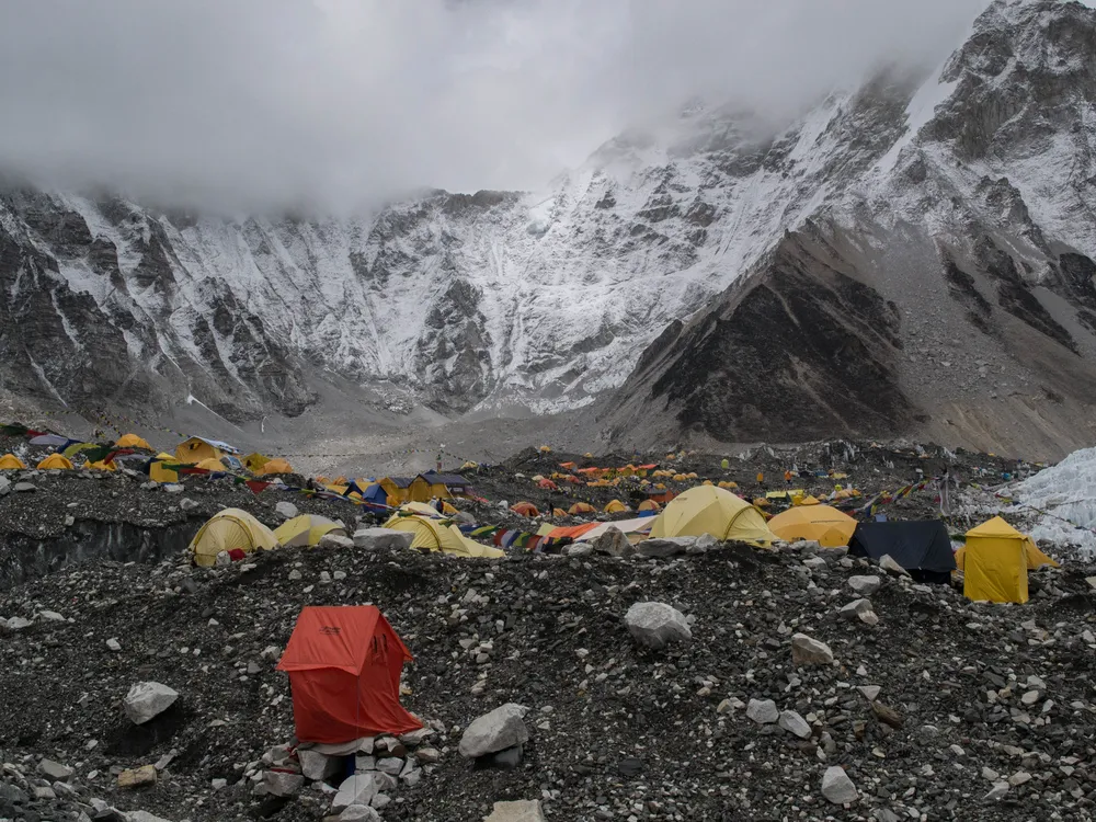 yellow and orange tents dot a rocky mountainside with peaks in the background obscured by storm clouds