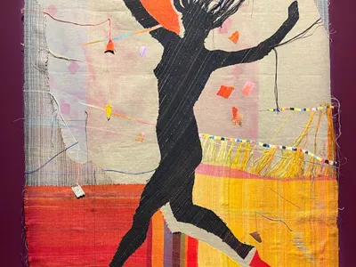 A black silhouette of a jumping woman against a colorful fabric background.